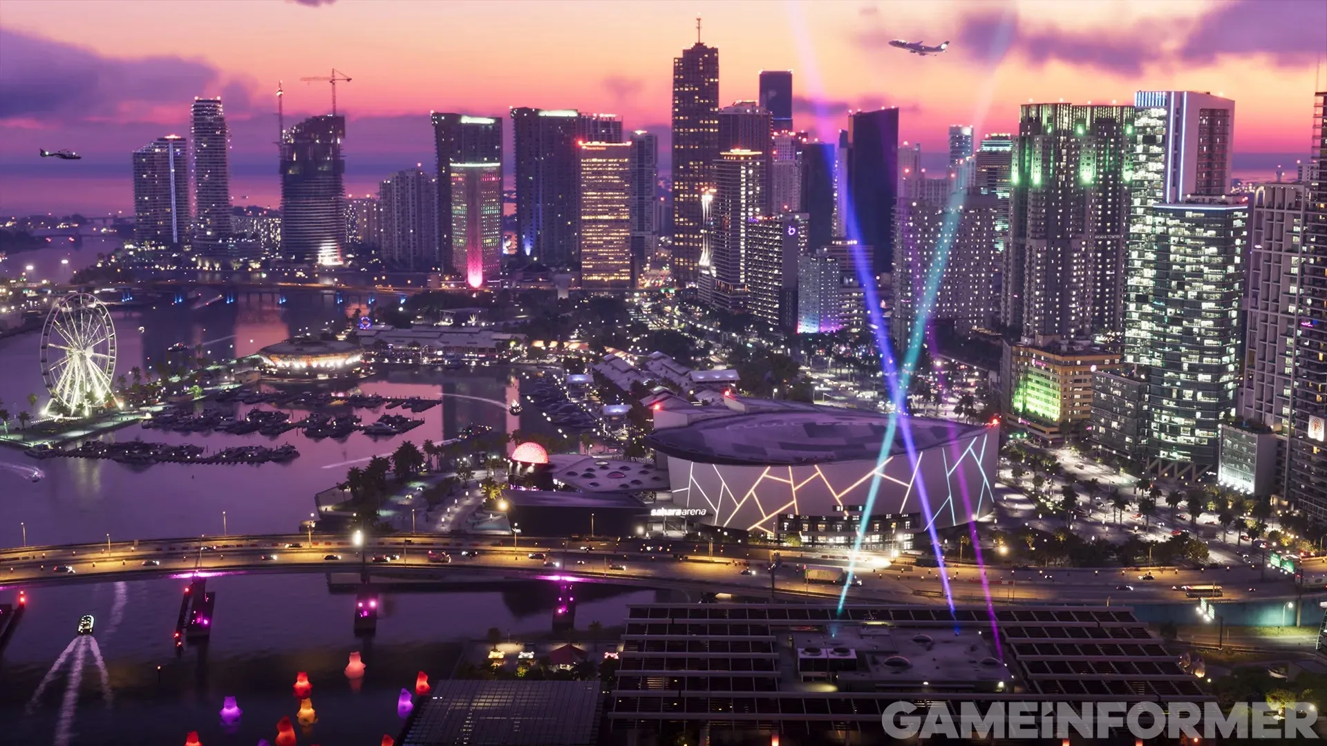 Vice City in der Dämmerung von oben, mit einer beleuchteten Arena, einem Riesenrad am Wasser und Wolkenkratzern unter einem violetten Himmel.