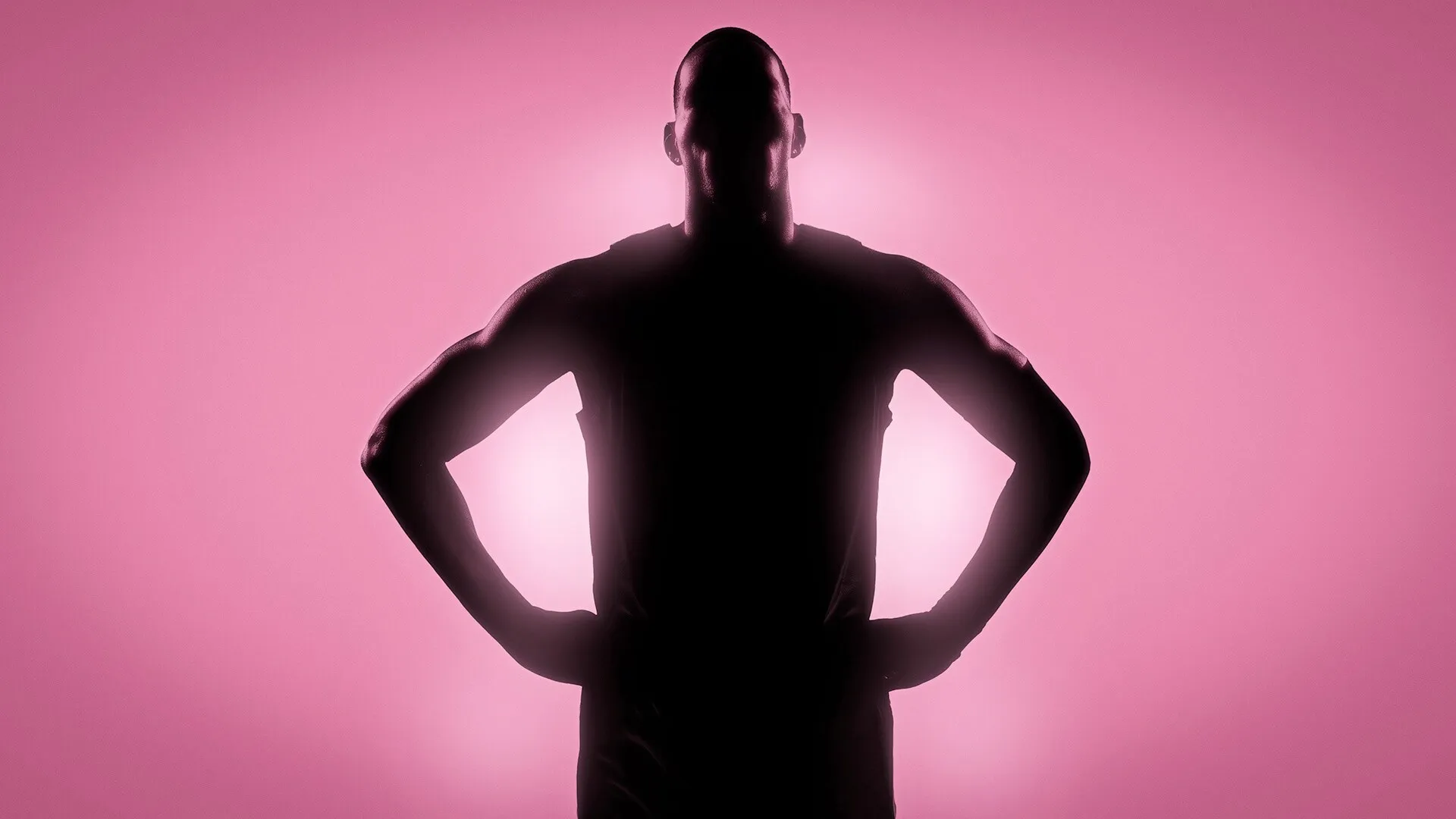 La silueta oscura de un jugador de baloncesto con las manos en la cintura, sobre un fondo rosa.