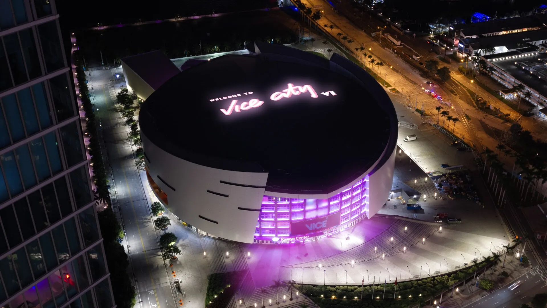 El Kaseya Center de noche visto desde el aire, con Welcome to Vice City VI iluminado en el techo y luz rosa alrededor de la entrada.