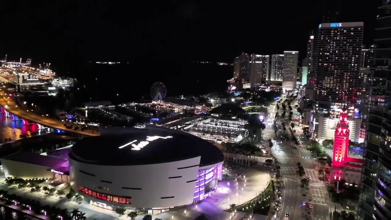 Miami bei Nacht aus der Luft, vorne das Kaseya Center mit dem Vice-City-Schriftzug auf dem Dach, ein Riesenrad an der Bucht und rechts ein roter Turm.