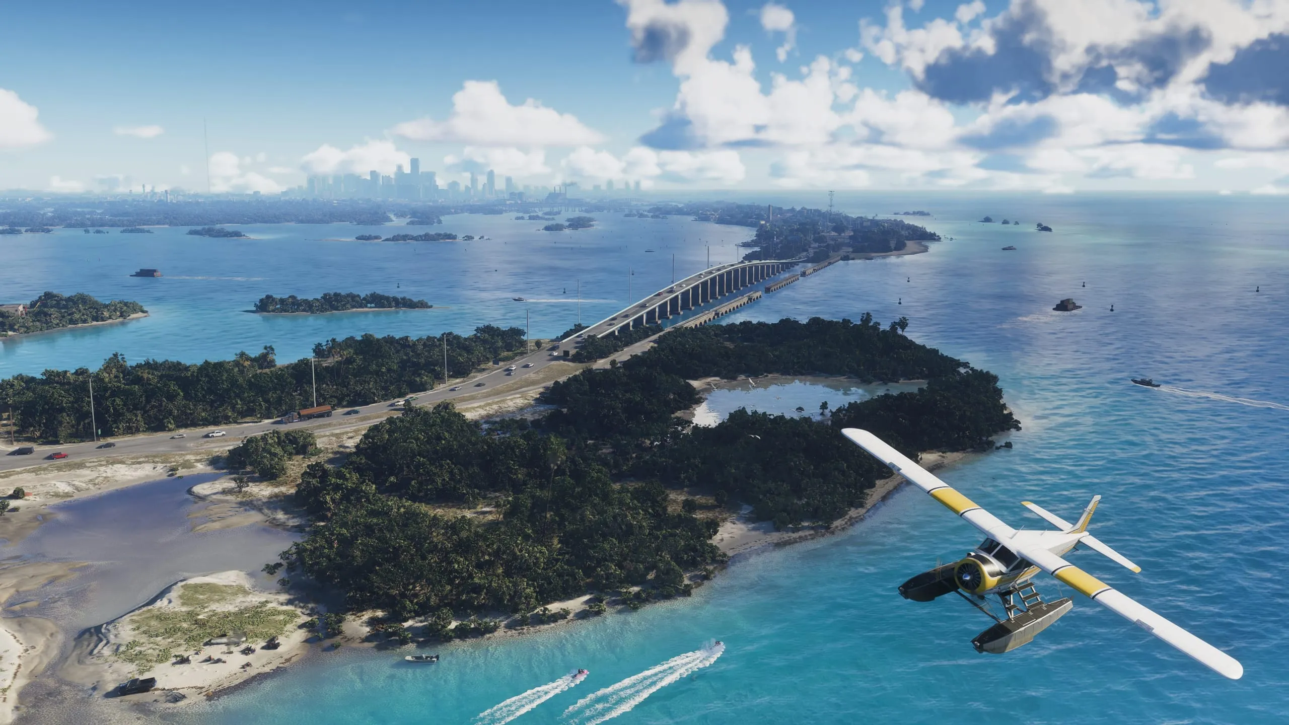 A seaplane flies over green islands in clear blue water, with a long bridge running towards the skyline of a city on the horizon.